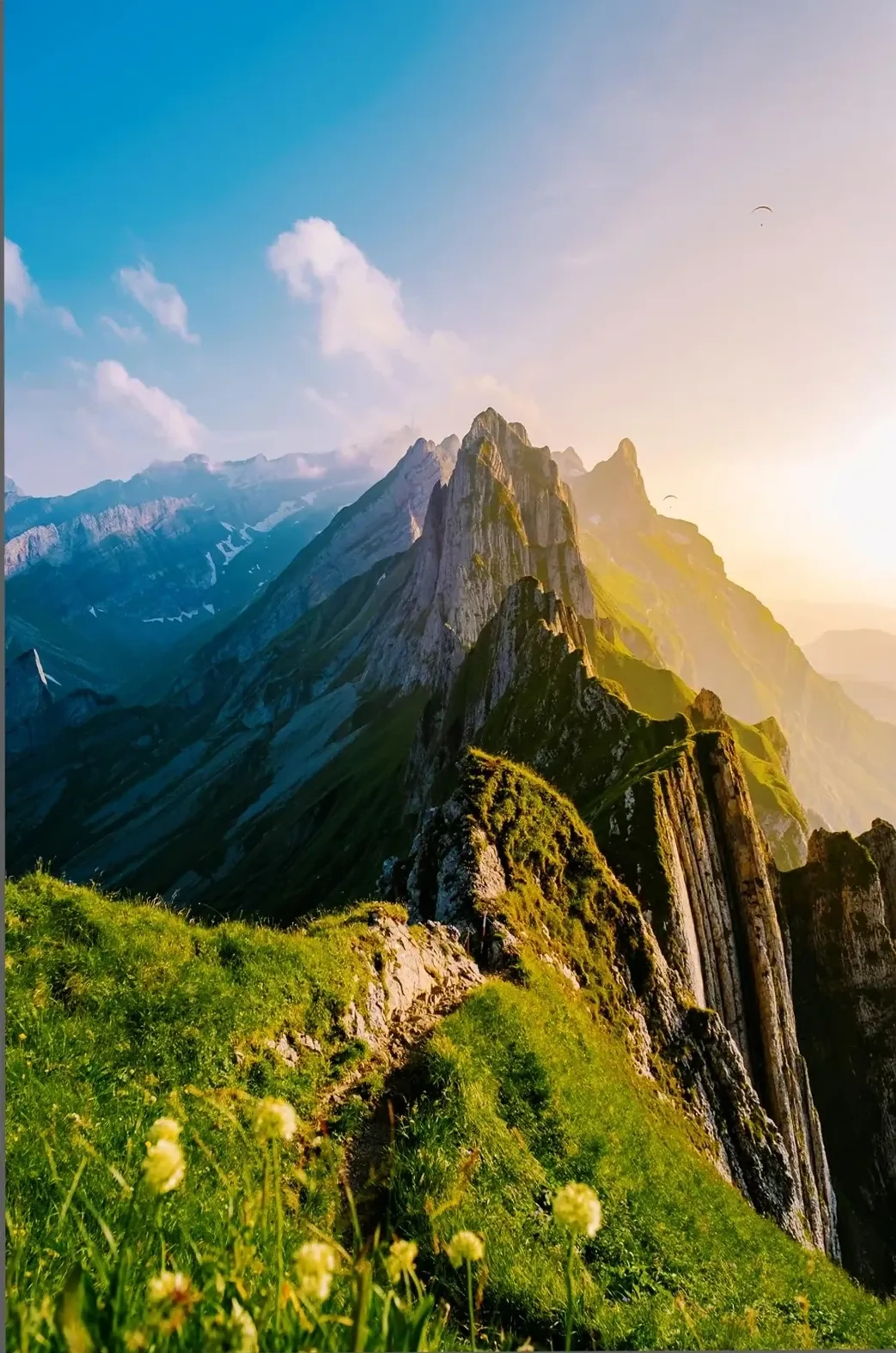 Ein schmaler Pfad verläuft über einen grünen Berggrat zu Felsspitzen im warmen seitlichen Sonnenlicht.