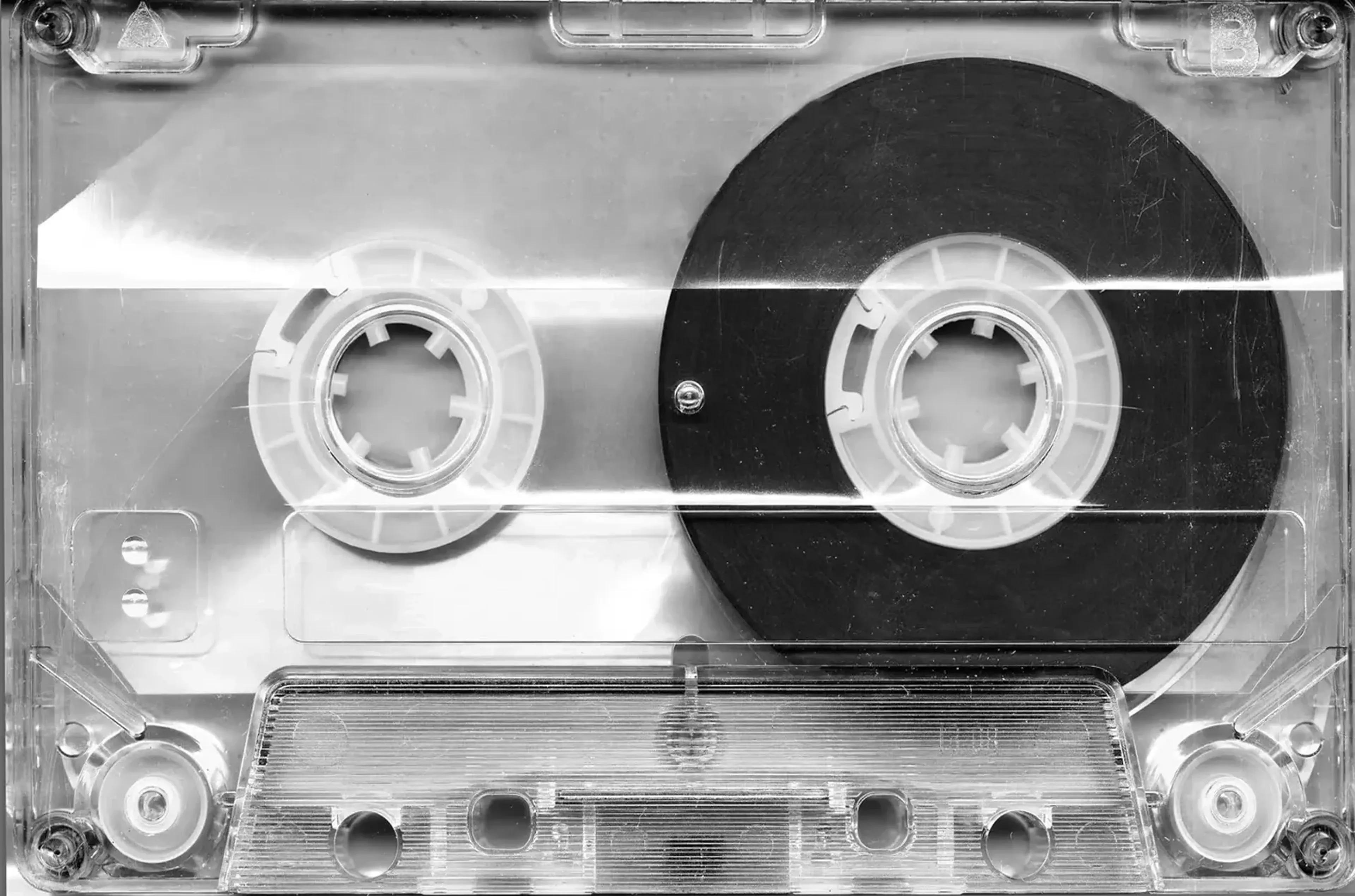 Durchsichtige Musikkassette in Schwarz-Weiß mit zwei hellen Spulen und einer großen dunklen Tonbandrolle rechts.