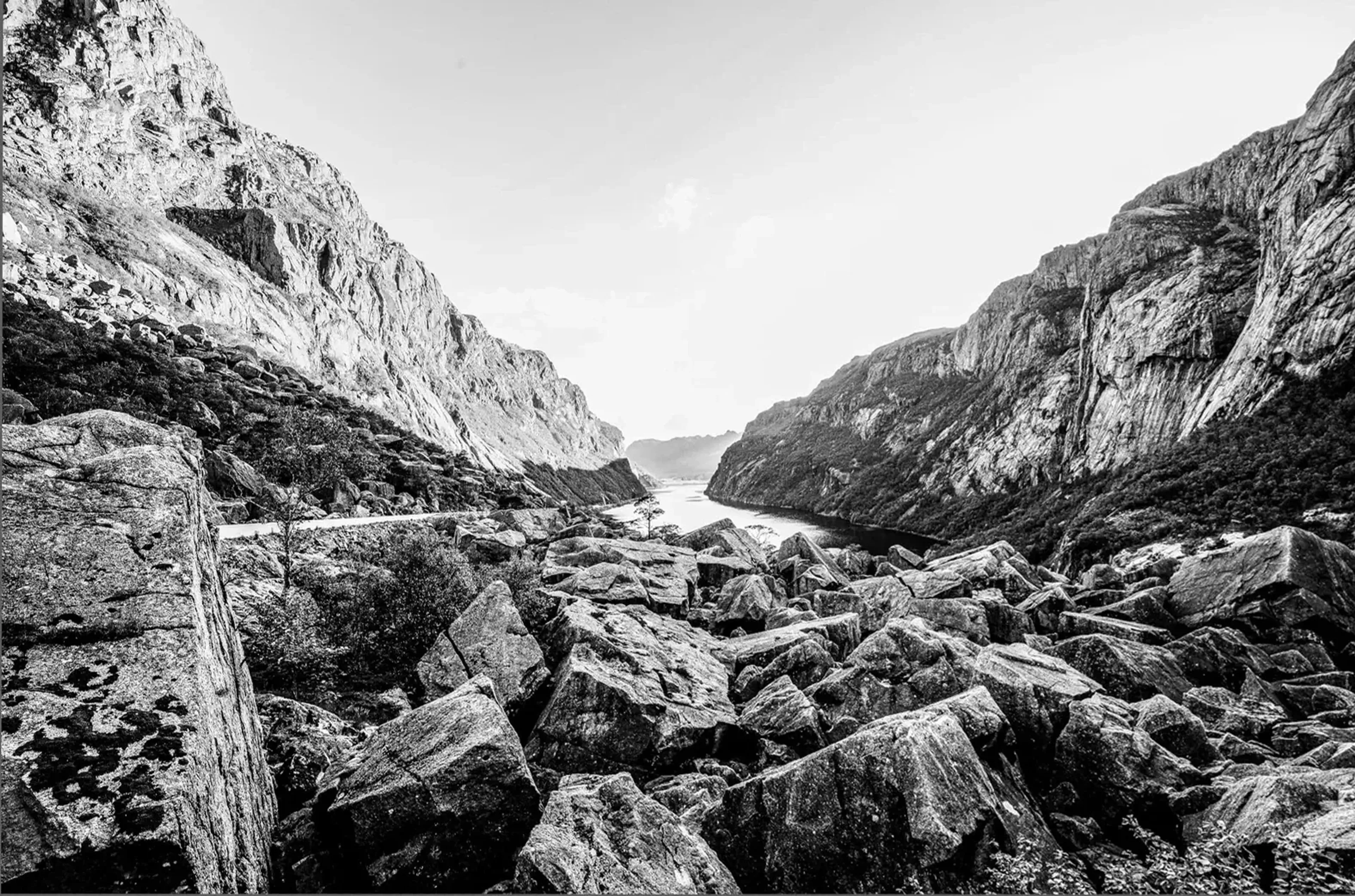 Schwarzweiße Felslandschaft mit großen Steinblöcken und einem schmalen Gewässer zwischen steilen Bergflanken.