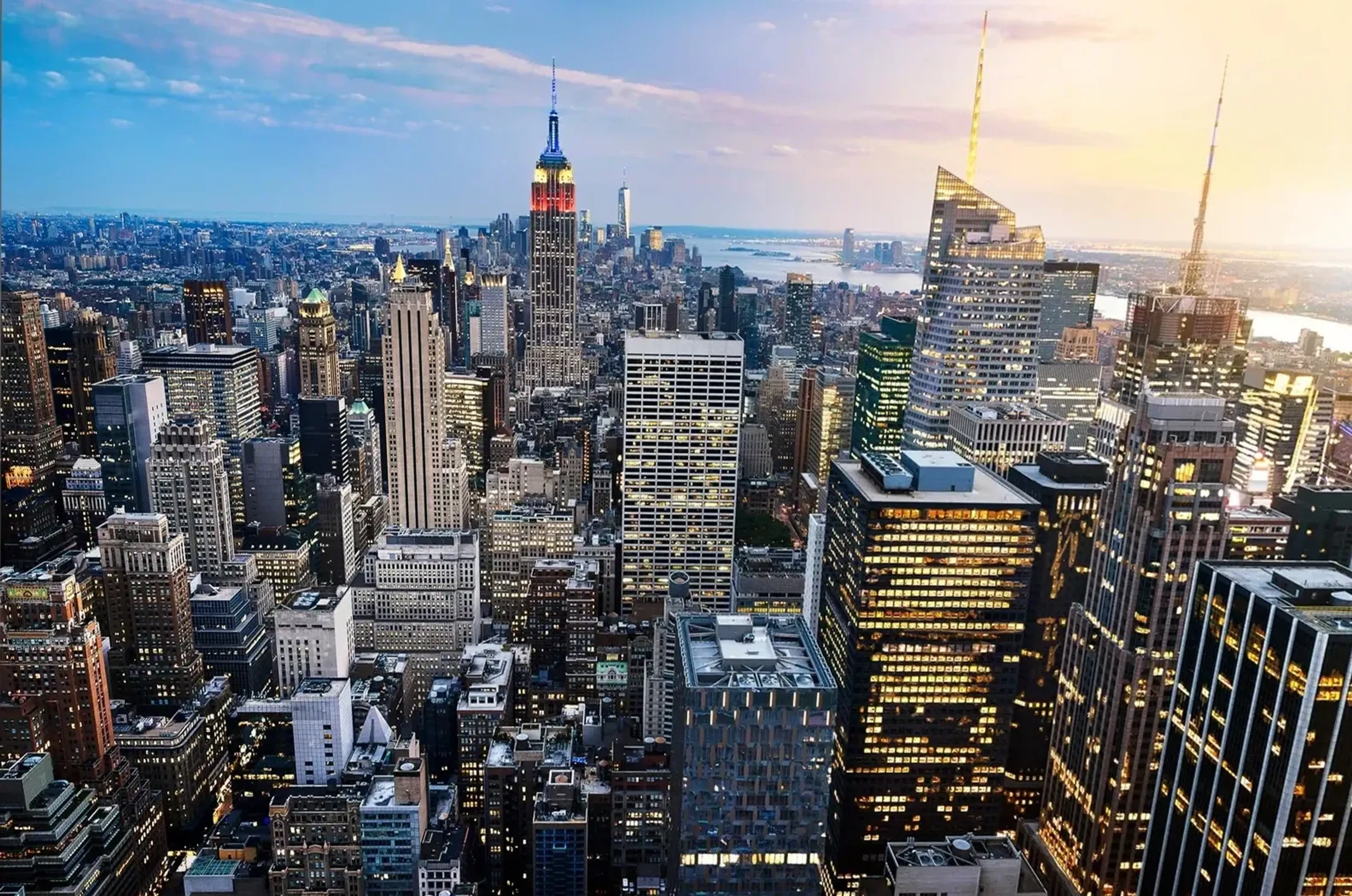 Blick über Manhattans dicht stehende Hochhäuser mit dem Empire State Building unter blau-gelblichem Himmel.