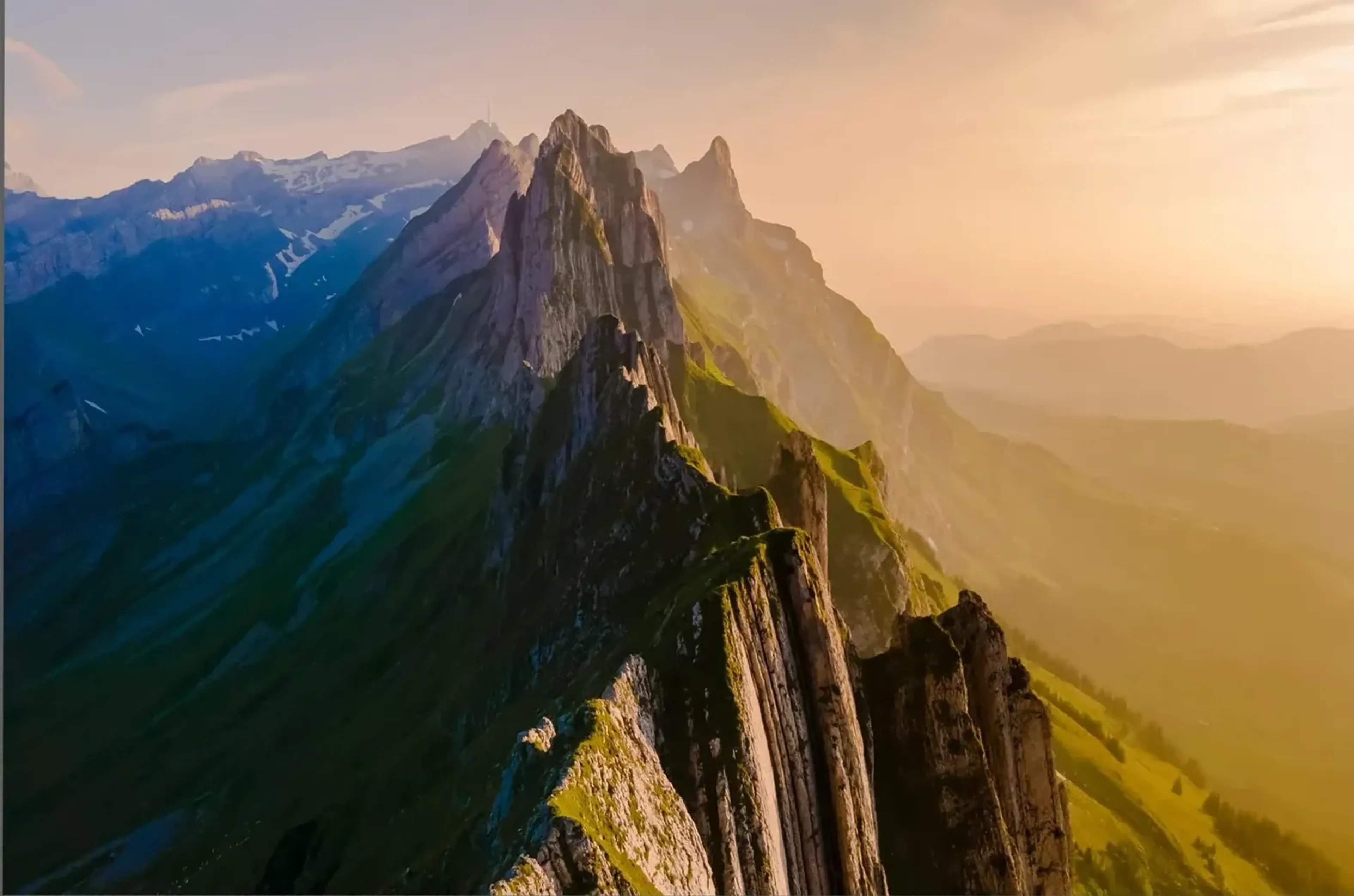 Ein felsiger Bergkamm mit grünen Hängen trennt kühle blaue Schatten links von goldenem Licht rechts.