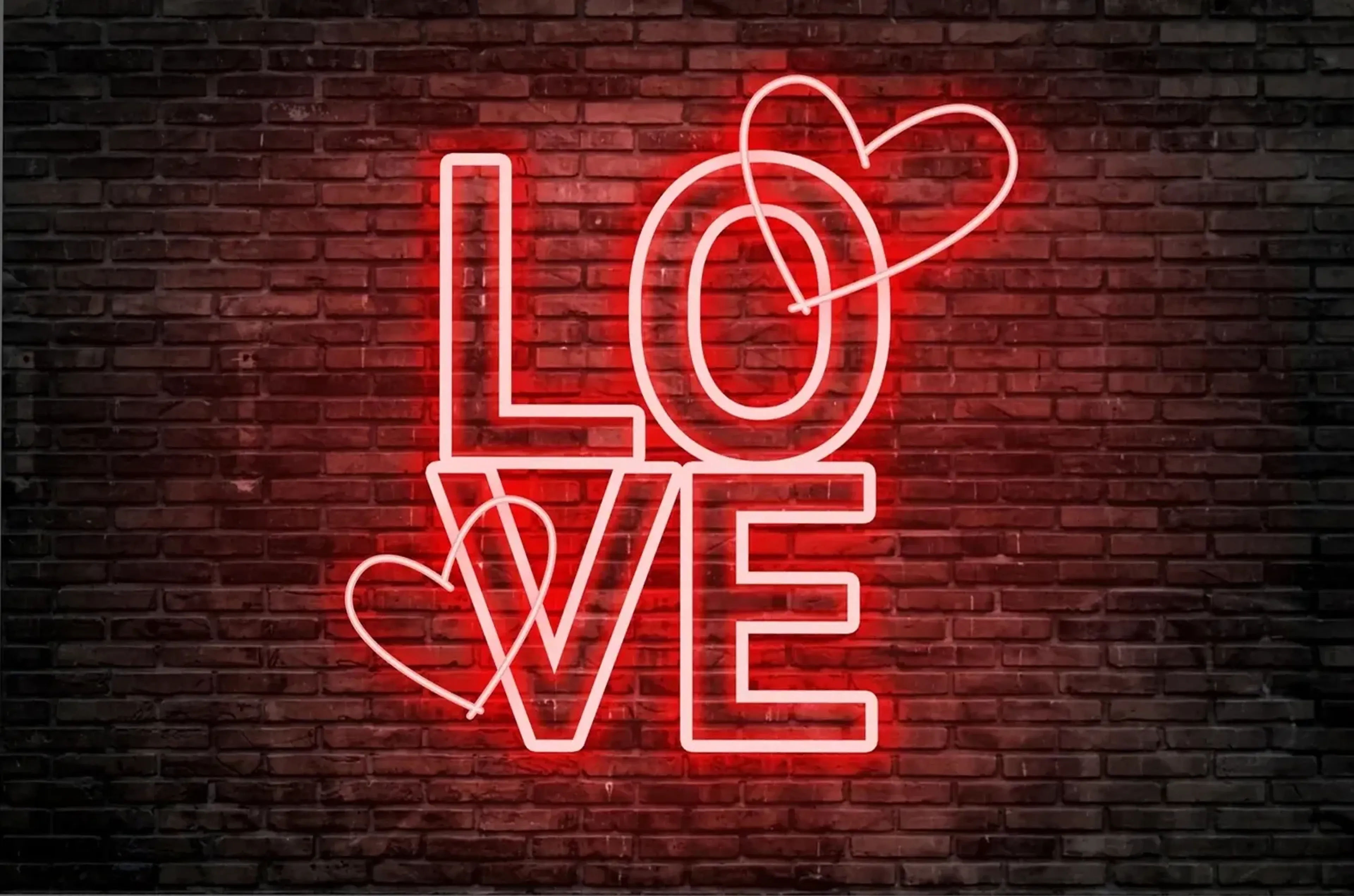 Rot leuchtender LOVE-Schriftzug in zwei Zeilen mit zwei Herzumrissen vor einer dunklen Backsteinwand.