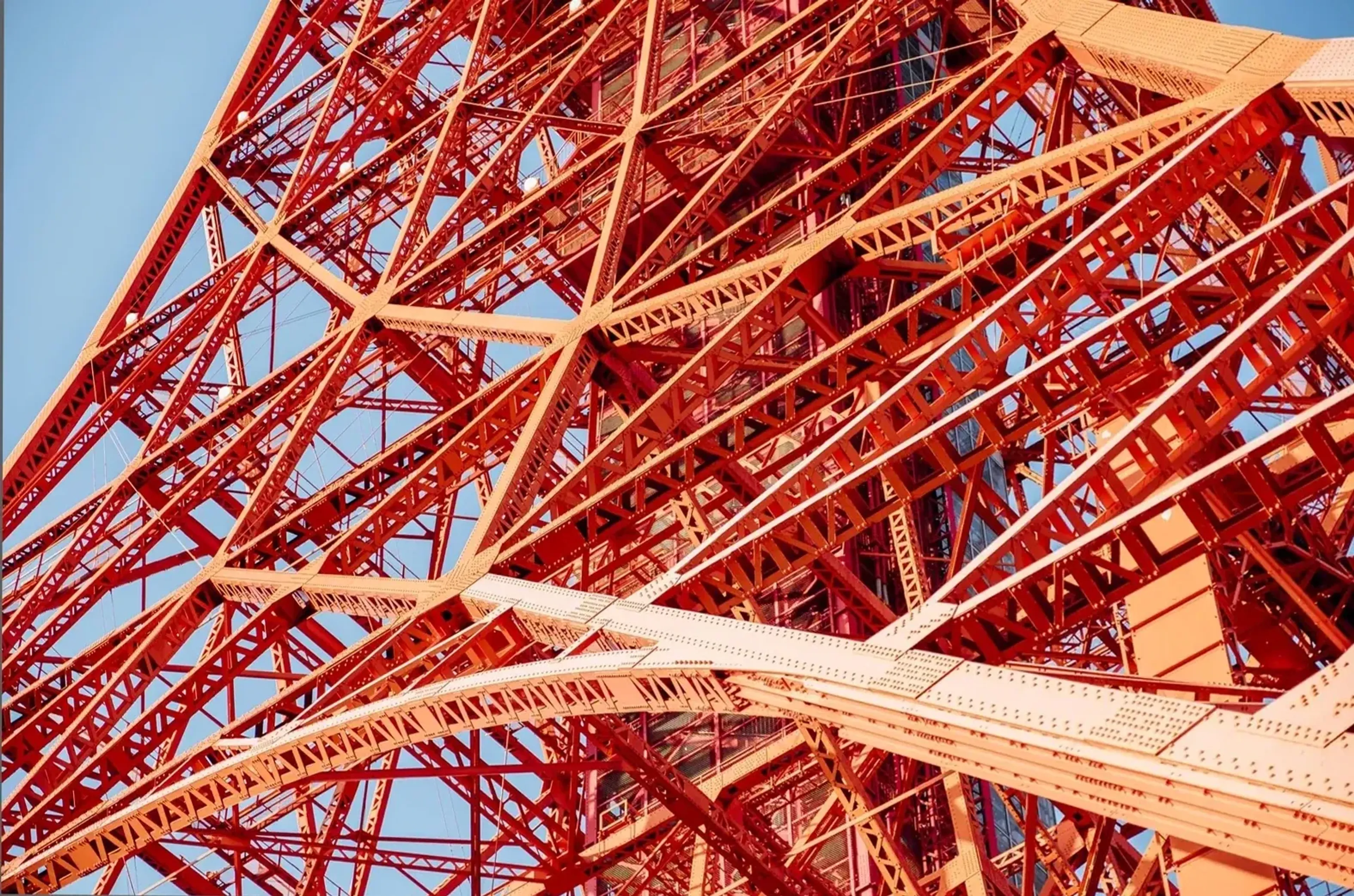 Rote und helle Streben, Treppen und Plattformen des Tokyo Tower kreuzen sich vor blauem Himmel.