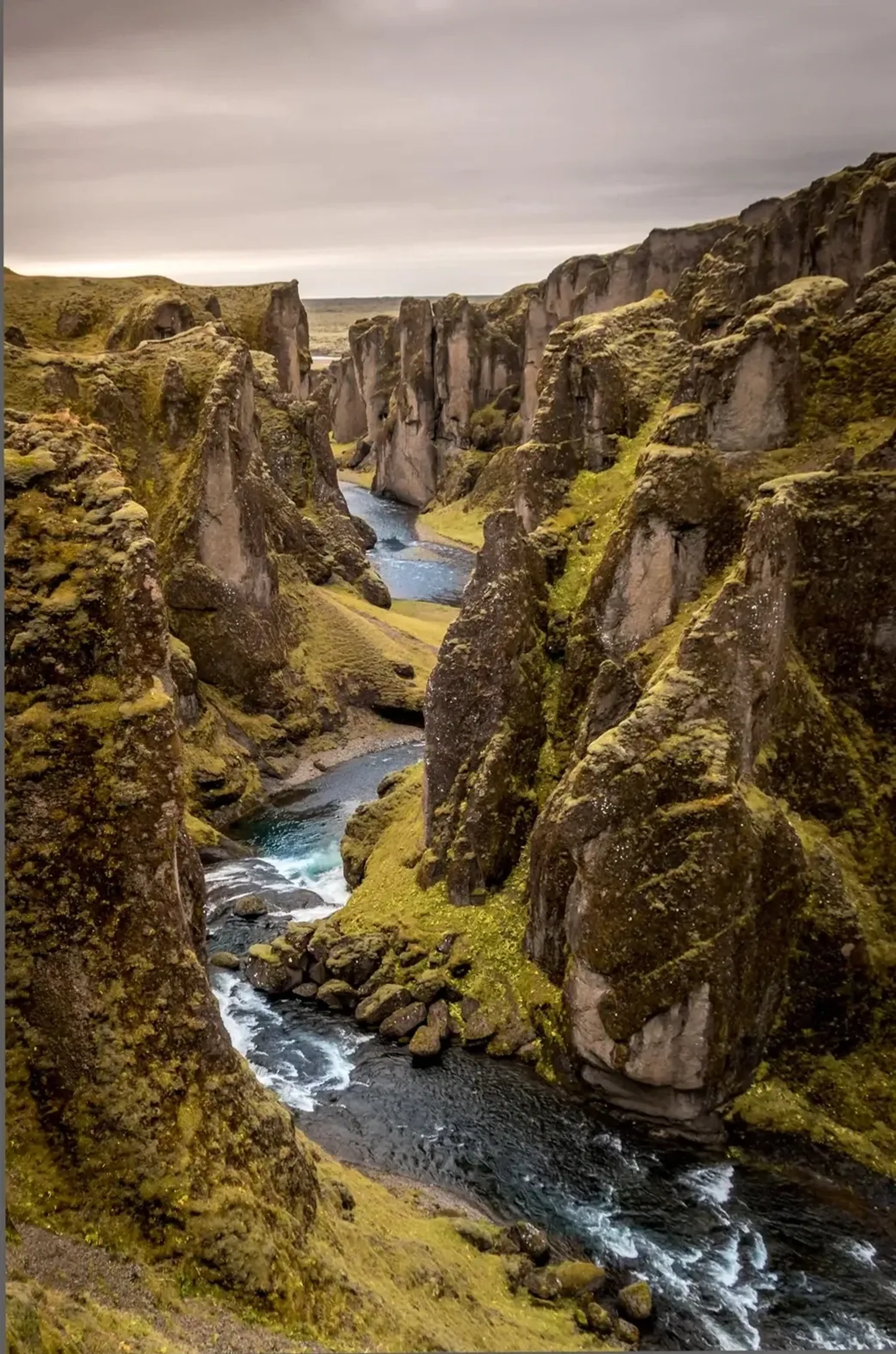 Ein schmaler Fluss mit weißen Strömungsspuren schlängelt sich durch eine tiefe Schlucht mit grün bewachsenen Felsen.