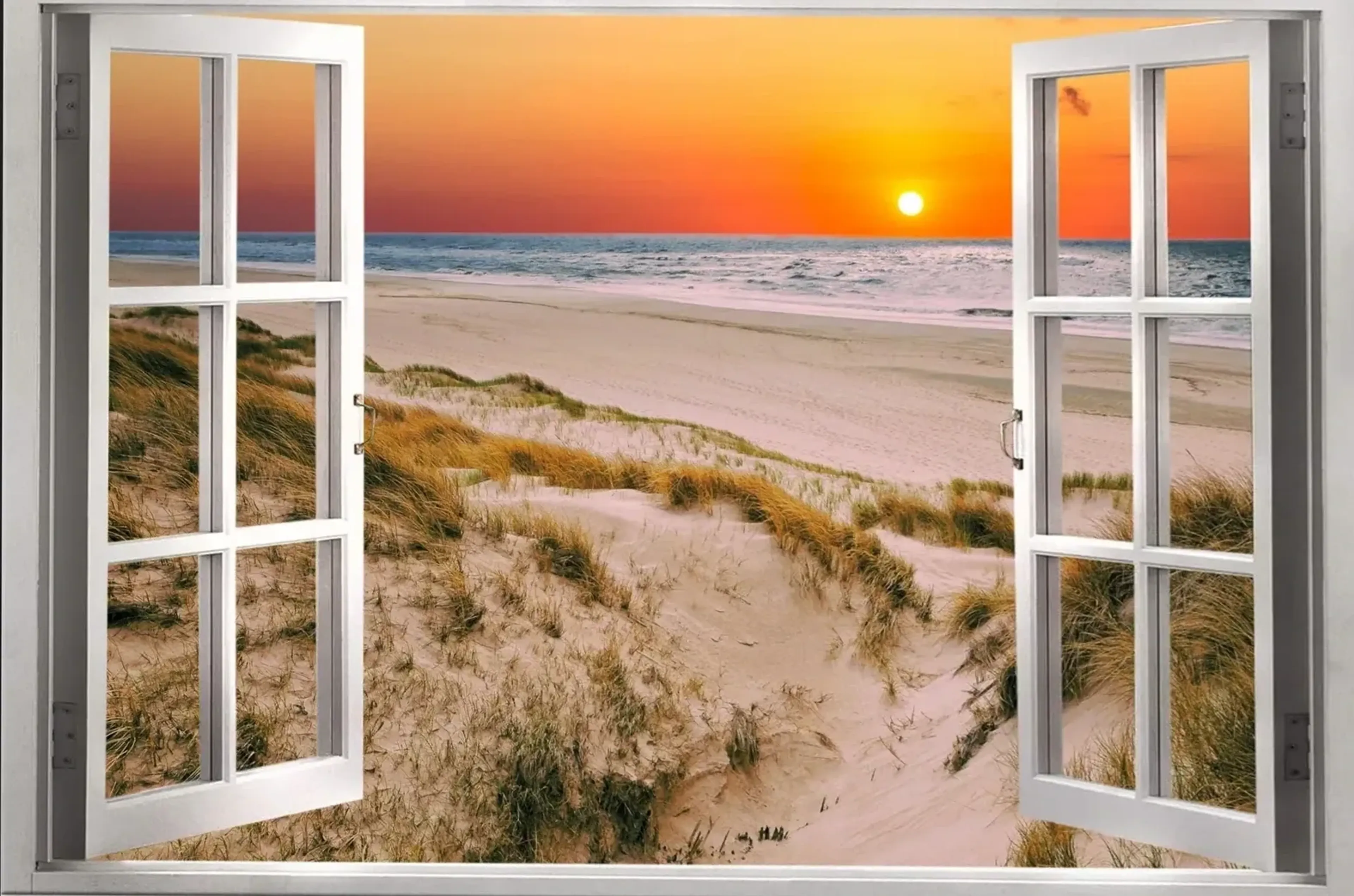 Offene weiße Fensterflügel rahmen Sanddünen mit Gras, einen Strand und das Meer bei tief stehender Sonne.
