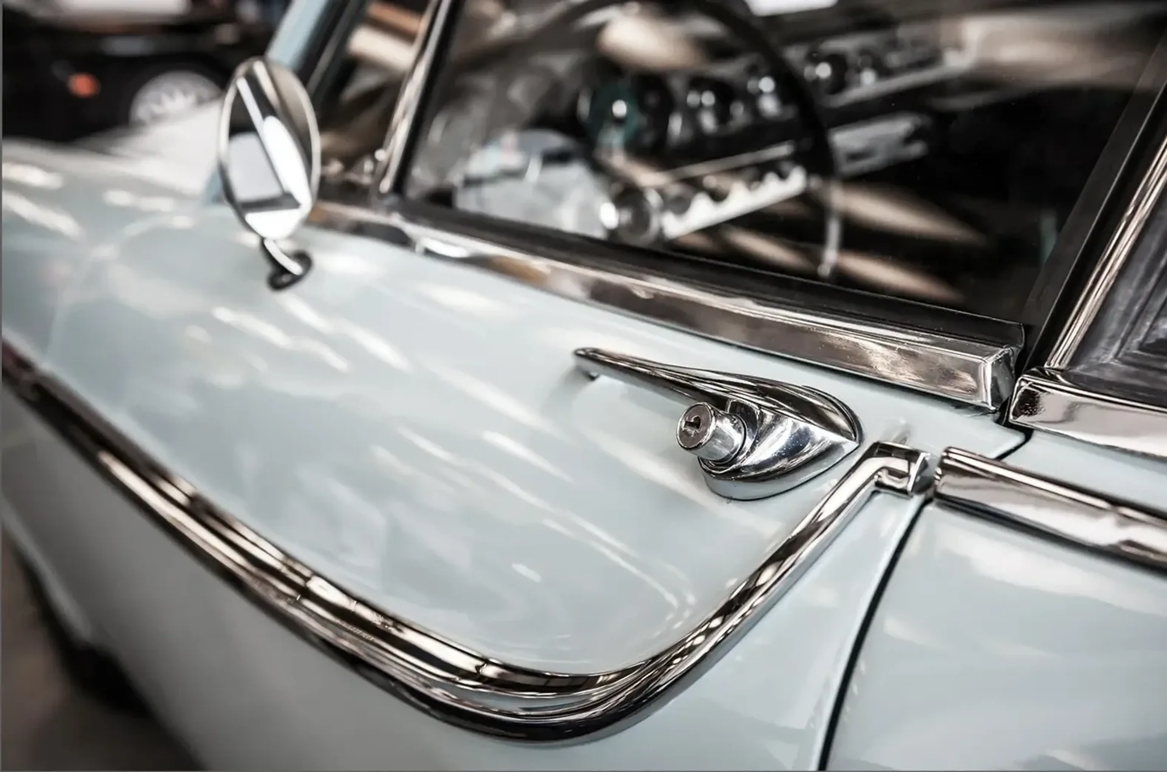 Hellblaue Oldtimertür mit glänzendem Griff, geschwungener Zierleiste und rundem Seitenspiegel.