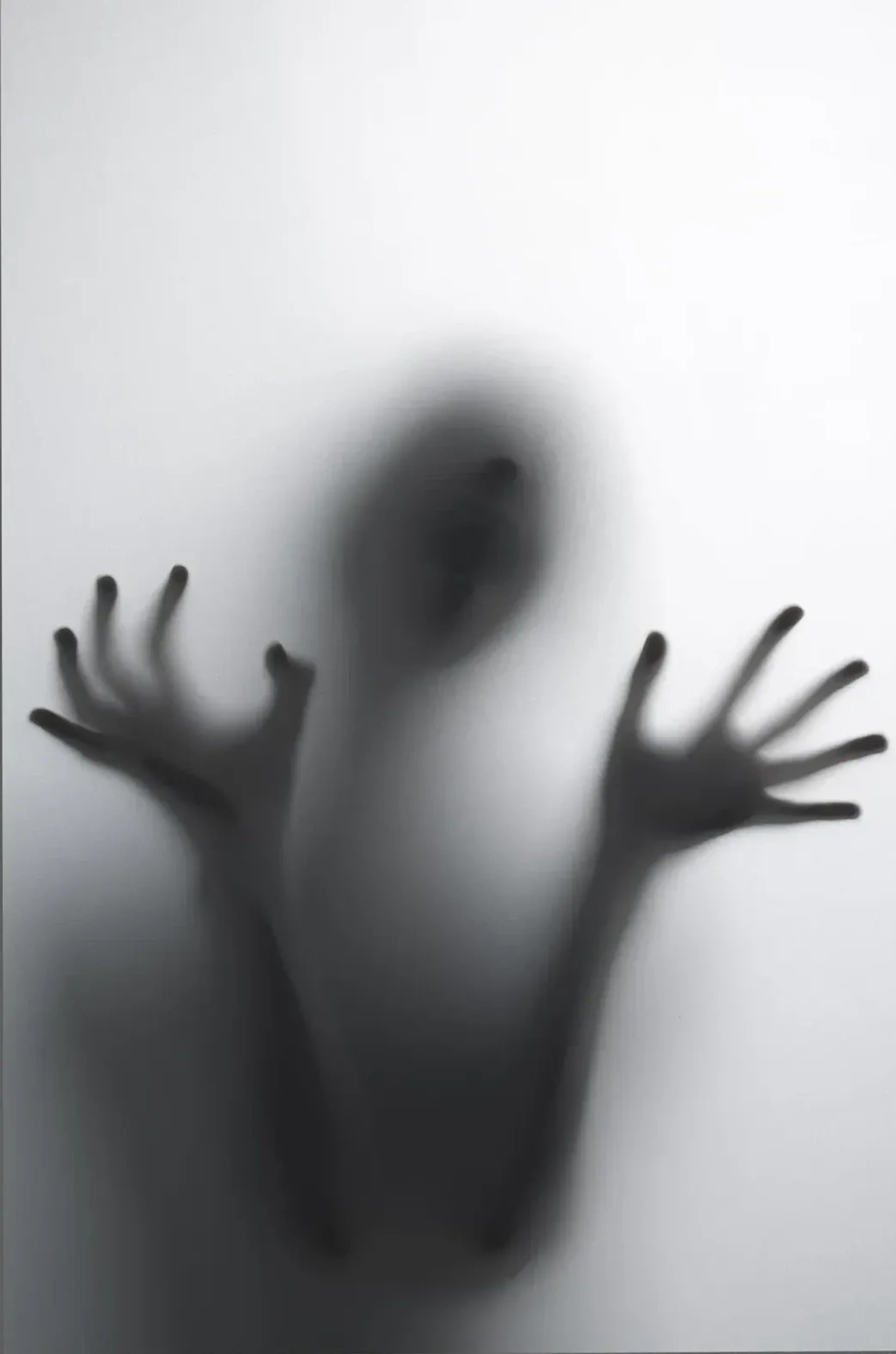 Dunkle Gestalt mit erhobenen Händen und gespreizten Fingern hinter einer hellen, matten Scheibe.